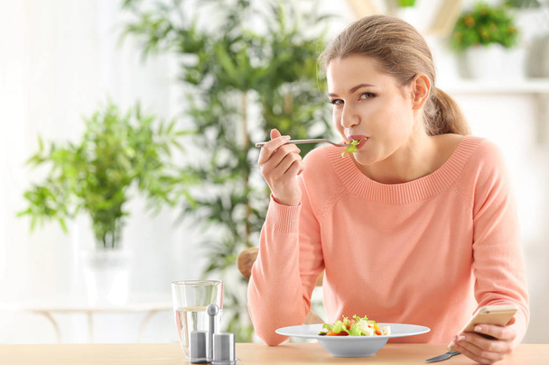 Young beautiful woman with phone eating fresh salad at home - Photo, image
