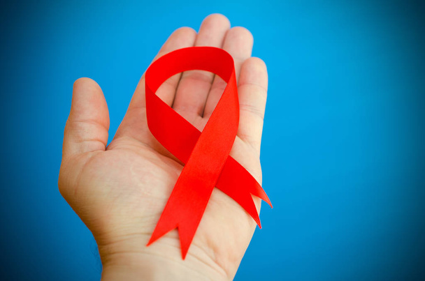 Red folded ribbon in hand on a blue background as a symbol of hemophilia. - Zdjęcie, obraz