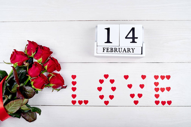 Valentines Day background with bouquet of red roses, sign Love from paper hearts and february 14 wooden block calendar, copy space. Greeting card mockup. Love concept. Top view, flat lay - Zdjęcie, obraz