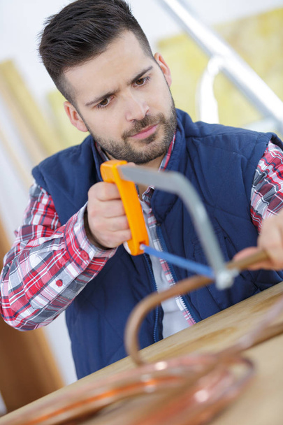 Hombre tratando de cortar la tubería de cobre con una sierra
 - Foto, Imagen