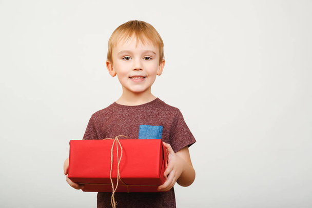 Happy cute little kid holding red gift box isolated over white background. - 写真・画像