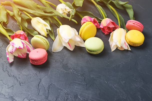 Makaroniki na czarnym tle i kolorowe tulipany. Miejsca na tekst. - Zdjęcie, obraz