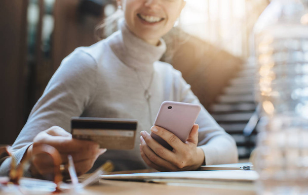Detail mladá usměvavá dívka drží kreditní kartu platit online v internetovém obchodě, zatímco sedí v moderní kanceláři - Fotografie, Obrázek