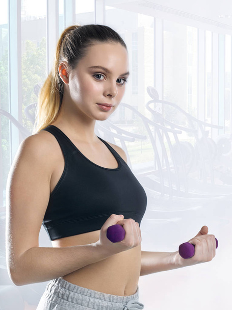 Beautiful young girl in a sport suit with purple dumbbells on th - Foto, Imagen