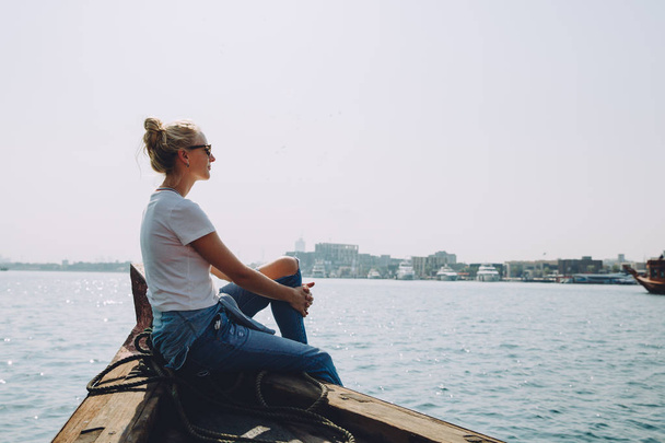 young beautiful blonde woman sitting at pier and looking at sea - Photo, Image