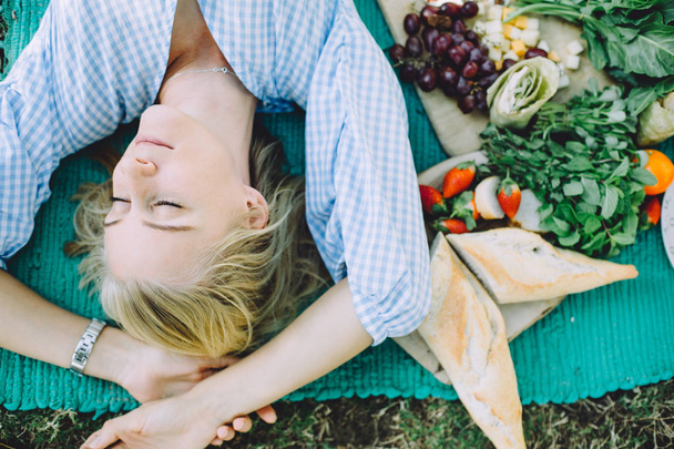 young woman relaxing at summer picnic lying on mat with healthy food  - Φωτογραφία, εικόνα