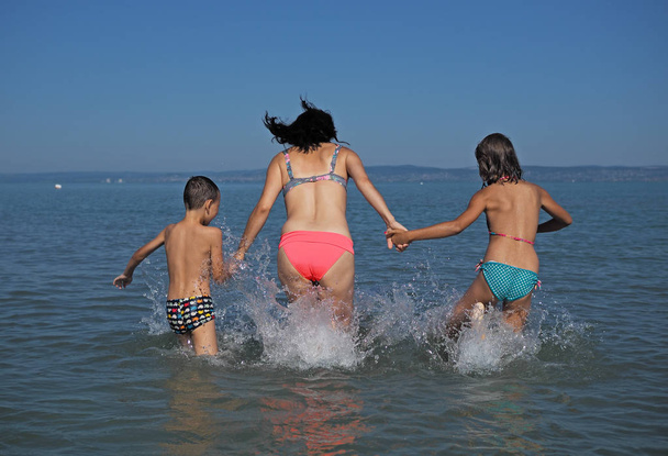 Mãe com seus filhos brincando na água
 - Foto, Imagem