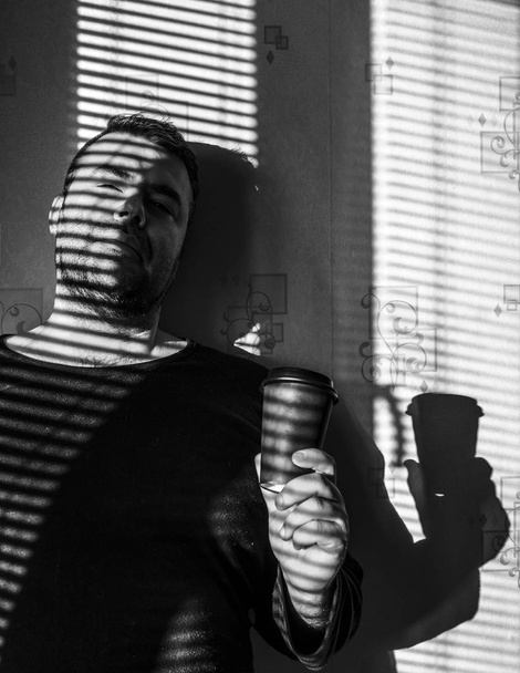 Paper cup of coffee in man's hand with  jalousie, shadow  - Zdjęcie, obraz