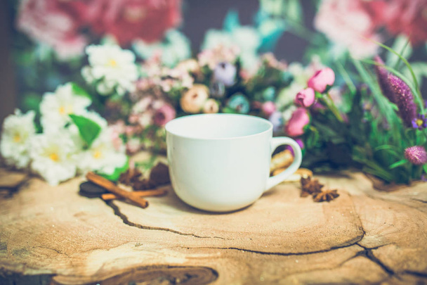 close-up of beautiful colored flowers with white cup of coffee on wooden background - Фото, изображение
