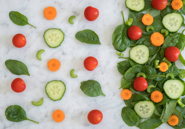 Modèle d'ingrédients de salade sur le dessus de banc de marbre, feuilles d'épinards bébé, carotte, tomates cerises, céleri et concombre faits en salade d'un côté
  - Photo, image