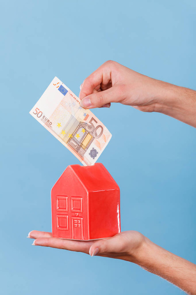 Person puts money into house piggybank - Φωτογραφία, εικόνα