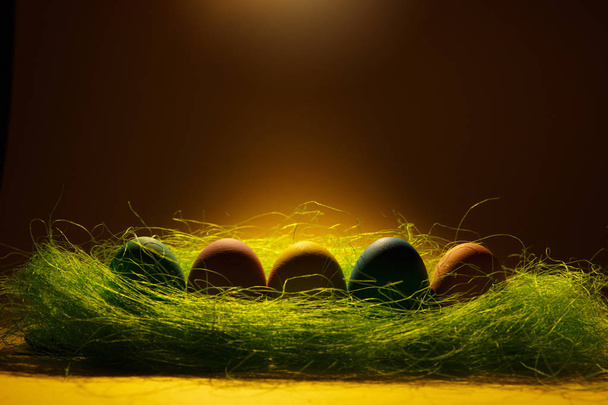 Fila de cinco coloridos huevos de Pascua pintados tradicionales monofónicos pastel en hierba verde sobre fondo amarillo oscuro con sombras negras, silueta, luz. Copia espacio para la publicidad. Con lugar para el texto
 - Foto, Imagen