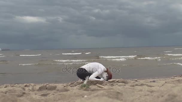 Kumlu deniz sahilinde beyaz boya kaplı sanatsal dişi çömelmiş - Video, Çekim