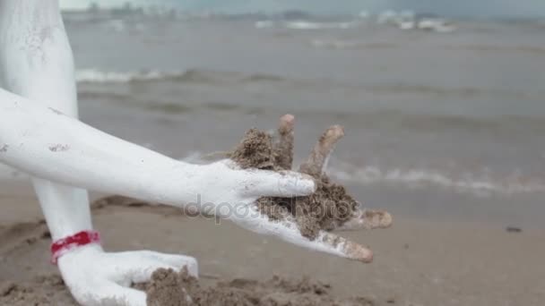 Herb Artystyczny woman, pokryte białą farbą chwyta mokry piasek na brzegu morza - Materiał filmowy, wideo