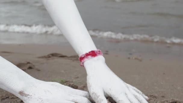 Herb Artystyczny Kobieta, pokryte białą farbą chwyta mokry piasek na brzegu morza - Materiał filmowy, wideo
