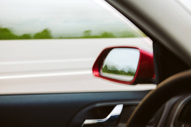 Defocused view of rearview mirror of a red fast driving car on highway - Foto, Imagem