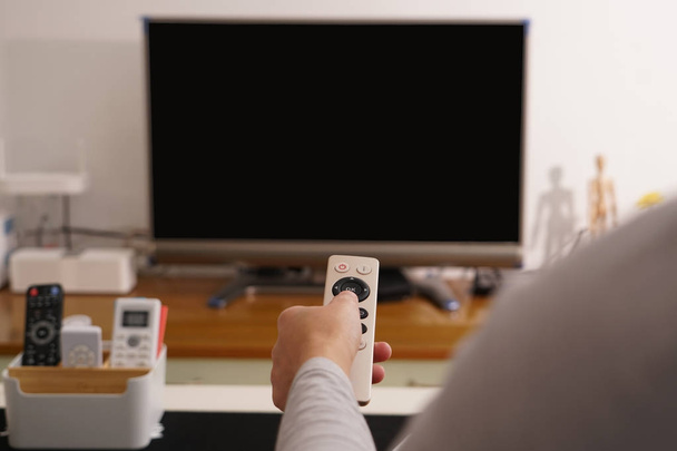 een vrouwen-hand houd de afstandsbediening van de Tv-kast in de woonkamer, het zwarte scherm Tv - Foto, afbeelding