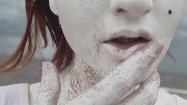 Artistieke meisje bedekt met witte verf Sleep vinger naar lippen op zee - Video