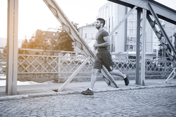 young sporty man jogging across the bridge at sunny morning in the city - 写真・画像