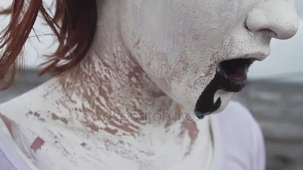 Ακτιβιστής καλλιτέχνη κορίτσι που καλύπτονται σε λευκό χρώμα drools μαύρο σούβλα στην ακτή θάλασσας - Πλάνα, βίντεο