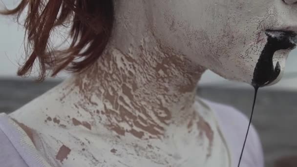 Activist kunstenaar vrouw bedekt met witte verf drools zwarte speeksel op zee - Video