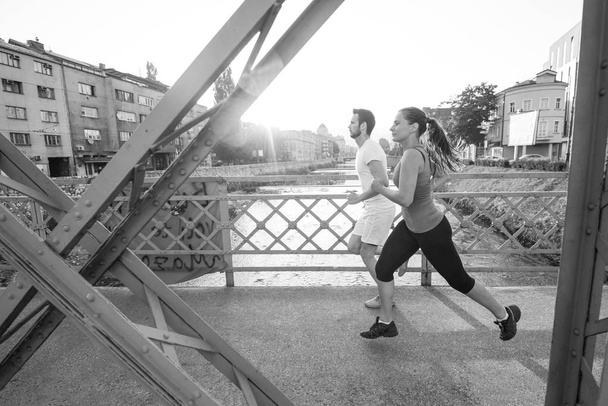 urban sports, healthy young couple jogging across the bridge in the city at sunny morning - Foto, afbeelding