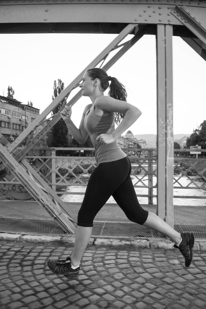 young sporty woman jogging across the bridge at sunny morning in the city - Foto, imagen