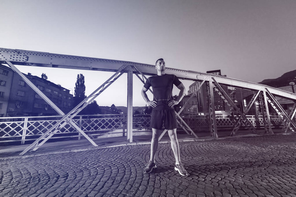 urban sports, young healthy man jogging across the bridge in the city at early morning - Foto, imagen