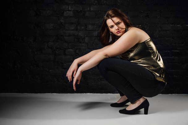 plus size model in a gold blouse and black jeans on a brick loft background. - Valokuva, kuva