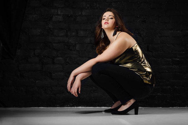 plus size model in a gold blouse and black jeans on a brick loft background. - Foto, imagen
