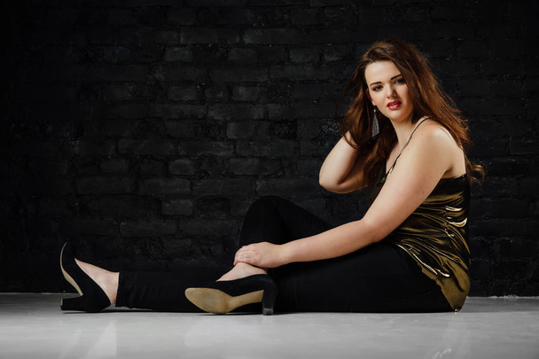 plus size model in a gold blouse and black jeans on a brick loft background. - Фото, зображення