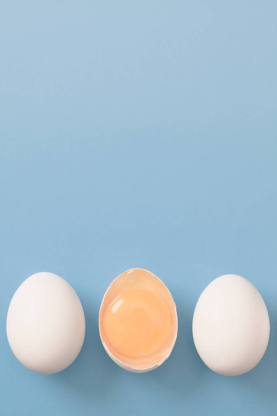 Biały jaja jest układanie w rzędzie, jeden z nich jest przedzielony trakcje i pokazuje żółtko.  - Zdjęcie, obraz
