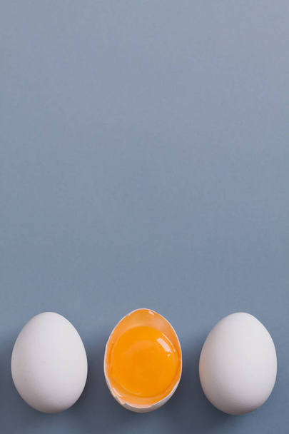 weiße Eier liegen hintereinander, eines davon ist zweigeteilt und zeigt Eigelb.  - Foto, Bild