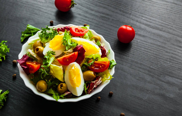 various fresh mix salad leaves with tomato, eggs and olive in bowl on dark wooden background - Φωτογραφία, εικόνα