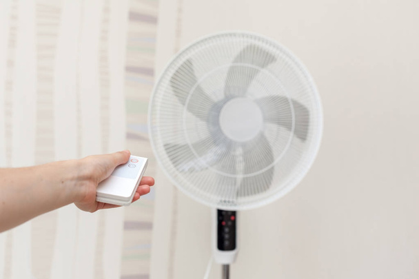 White electric fan turns on, turns off with the remote control. Hand hold electric fan remote. - Photo, Image