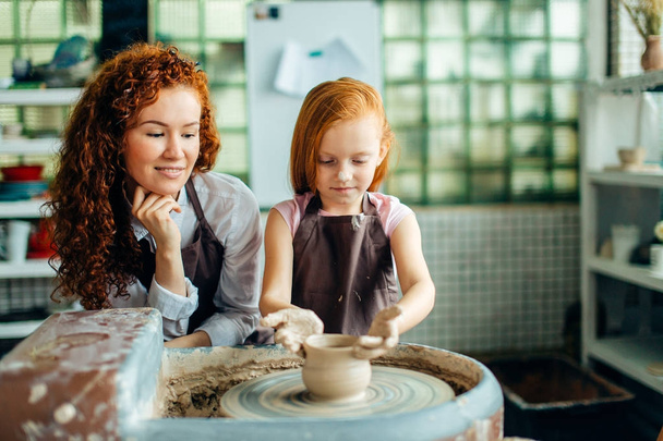 redhead mother and her child daughter moulding with clay on pottery wheel - Фото, зображення