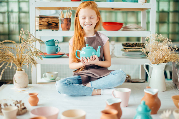 redhead girl sitting at clay workshop studio with many cup - Фото, изображение