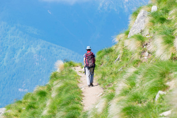 Backpacker walking on hiking trail in the mountain. Summer adventures summer vacation on the Alps. Wanderlust people traveling concept. - Photo, Image