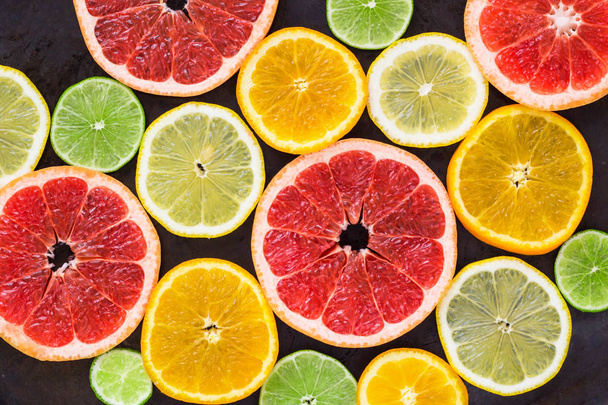 bovenaanzicht van segmenten van citrusvruchten op zwarte achtergrond - Foto, afbeelding