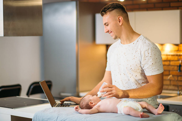 dad trying to work while standing with his newborn babe in home office interior - Photo, image