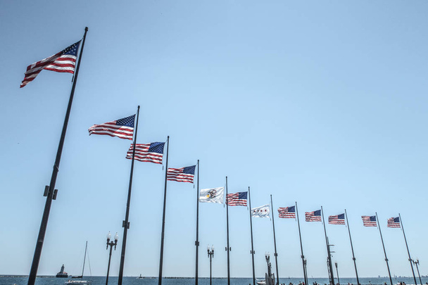 Chicago - 2 de julio de 2017: Una fila de banderas estadounidenses ondean orgullosamente al final del muelle de la Marina durante un cálido fin de semana festivo del 4 de julio en Chicago
. - Foto, imagen