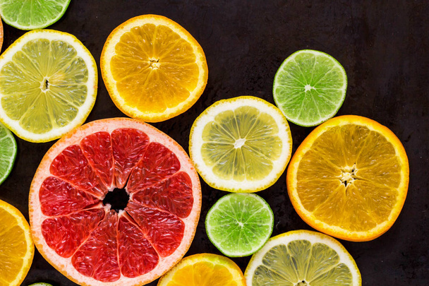 top view of slices of citrus fruits on black background. - Photo, Image