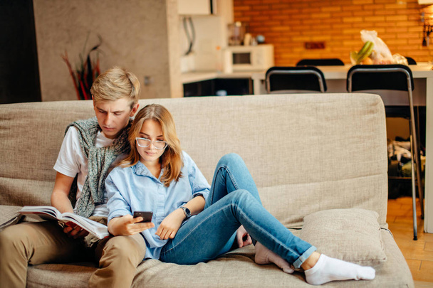 couple sitting on sofa, leisure together, man reading book, woman using phone - 写真・画像