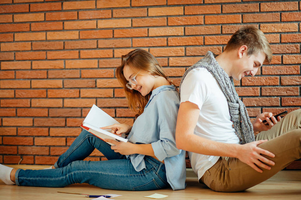 young couple reading a book sitting on wooden floor at home - Foto, afbeelding