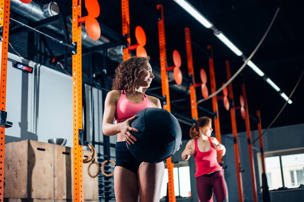 Two women throws medicine balls in fitness gym - 写真・画像