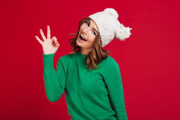 Happy brunette woman in sweater and funny hat showing ok - Fotoğraf, Görsel
