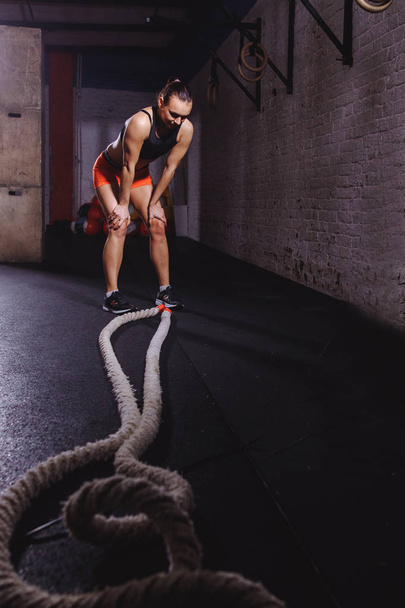 αθλήτρια στέκεται στο γυμναστήριο μετά από την προπόνηση σχοινί μάχη και κοιτάζοντας προς τα κάτω - Φωτογραφία, εικόνα