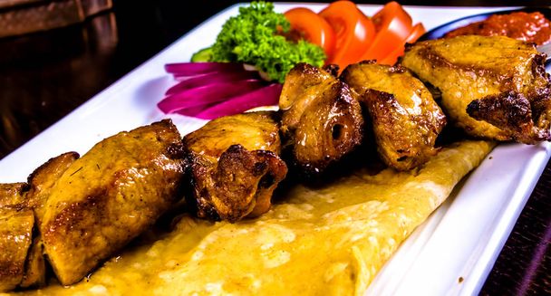 Shish kebab on skewer with flatbread and vegetables on white plate - Photo, Image