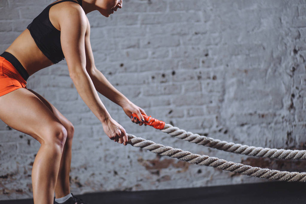 close up photo of Athletic woman doing battle rope exercises at gym - 写真・画像