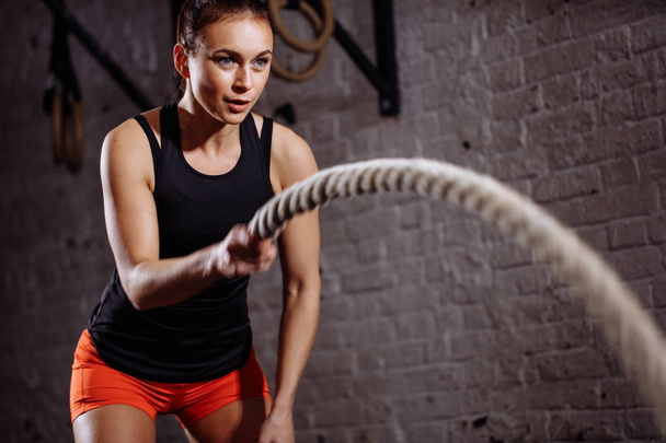 close up photo of woman doing Battle rope workout near white brick wall - Photo, image